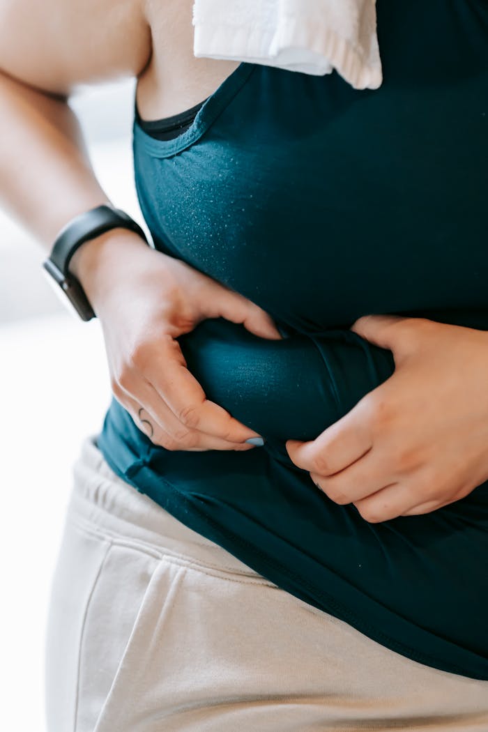 Crop faceless plus size female demonstrating problem with overweight by evaluating quantity of excess fat on stomach